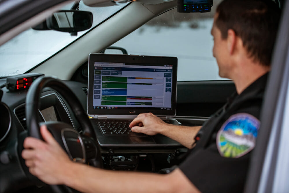 Police officer in vehicle using law enforcement software and systems